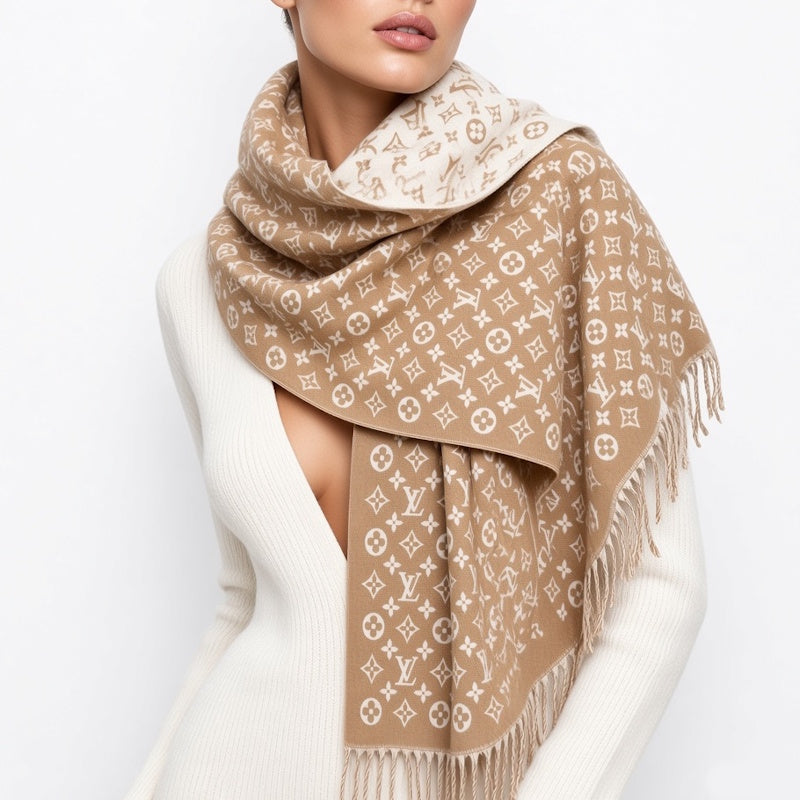 A beige and white monogram scarf with fringe, wrapped around a model wearing a white ribbed sweater against a light gray background.