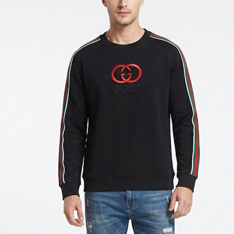 A man wearing a black Gucci crewneck sweatshirt with red and green stripe details on the sleeves and a red interlocking G logo on the chest, paired with blue jeans against a white studio background.