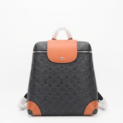 A LU monogram backpack in black coated canvas with tan leather accents on the front flap, bottom corners, and top handle, shown against a plain white background.