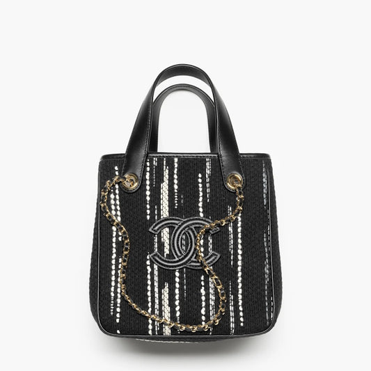 A black woven handbag with vertical white textured stripes, black leather handles, a gold-tone chain strap, and a prominent interlocking CC logo on the front, set against a plain white background.