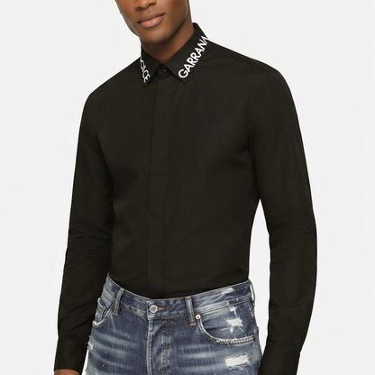 A man wearing a black long-sleeve button-down shirt with 'GARRAN' printed in white on the collar, paired with distressed blue jeans, against a light gray background.