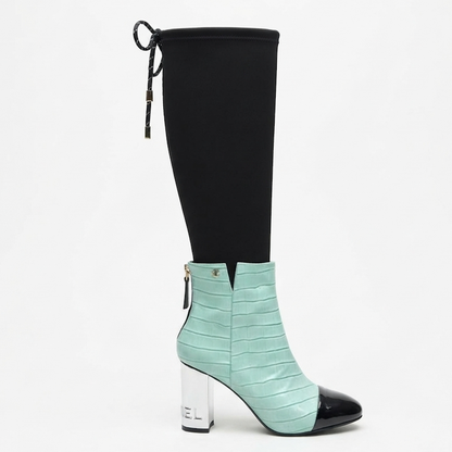 A knee-high boot with a black fabric upper and a mint green crocodile-embossed ankle bootie with a black pointed toe and a clear block heel.