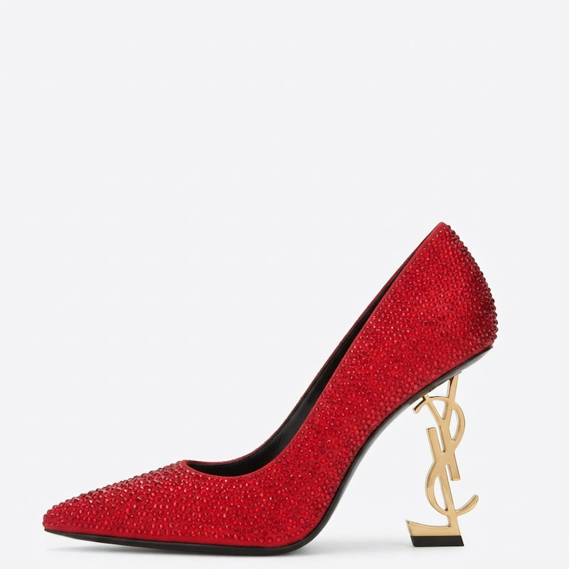 A red high-heeled pump shoe covered in sparkling rhinestones, featuring a gold-tone Y L monogram heel and a pointed toe, shown against a plain white background.