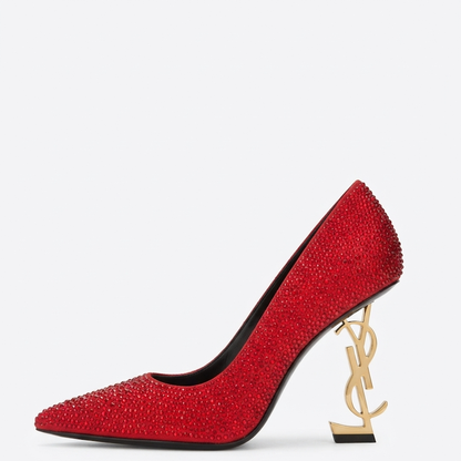 A red high-heeled pump shoe covered in sparkling rhinestones, featuring a gold-tone Y L monogram heel and a pointed toe, shown against a plain white background.