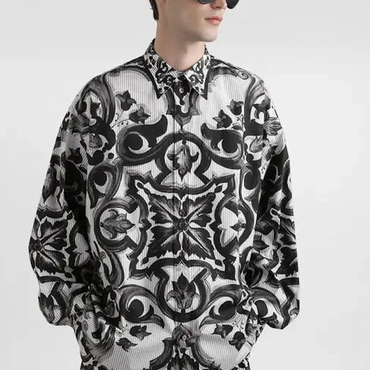 A man wearing a long-sleeve button-up shirt with an intricate black and white baroque-style ornamental pattern, shown against a plain light gray background.