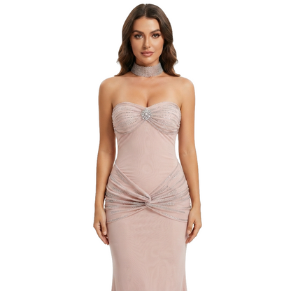 A woman modeling a strapless blush pink evening gown with a sweetheart neckline, embellished beading on the bodice, a matching beaded choker, and a ruched twist detail at the waist.