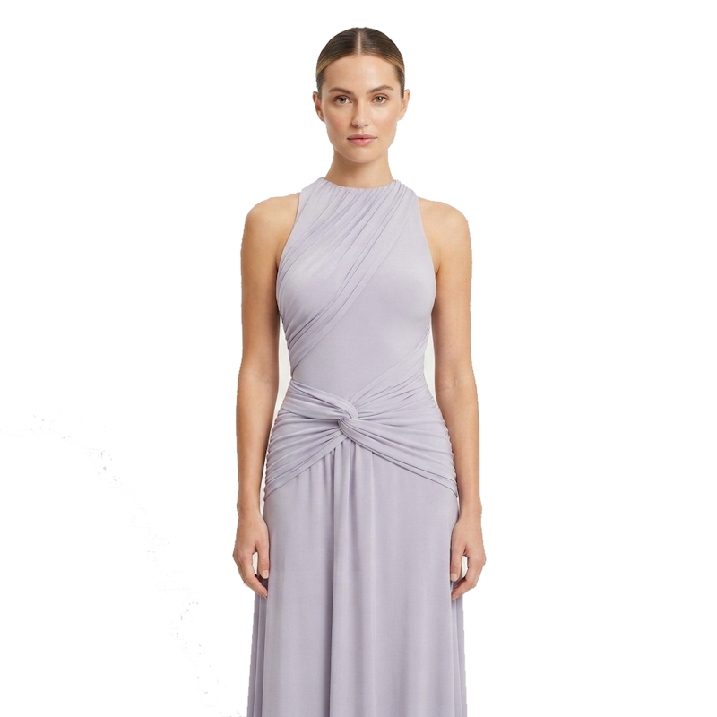 A woman modeling a sleeveless, high-neck, floor-length gown in a light lavender-gray color, featuring draped detailing and a twisted knot at the waist, set against a plain white background.