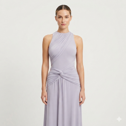 A woman modeling a sleeveless, high-neck, floor-length gown in a soft lavender-purple color. The dress features draped detailing across the bodice and a twisted knot at the waist, set against a plain light gray studio background.