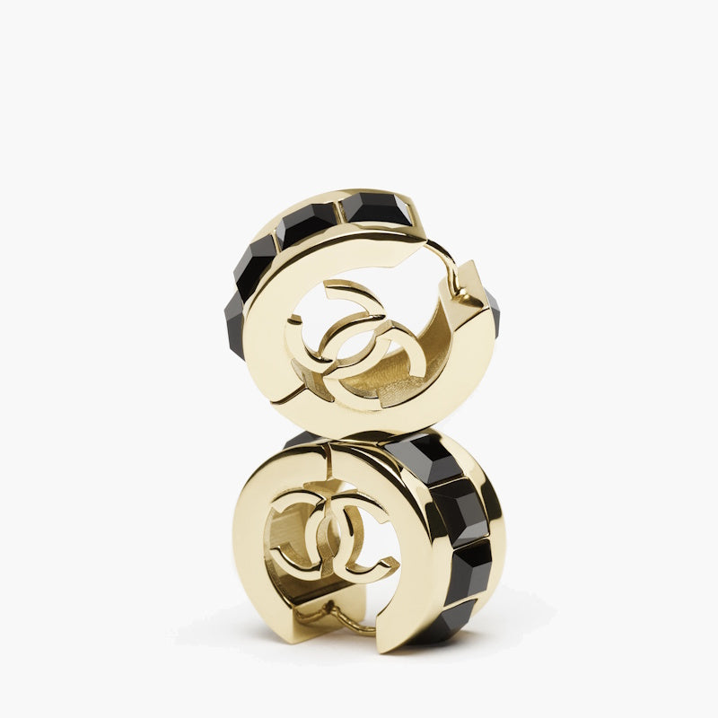 A pair of gold-tone huggie hoop earrings with black faceted crystal inlay, featuring a cutout interlocking CC logo design, shown on a clean white background.