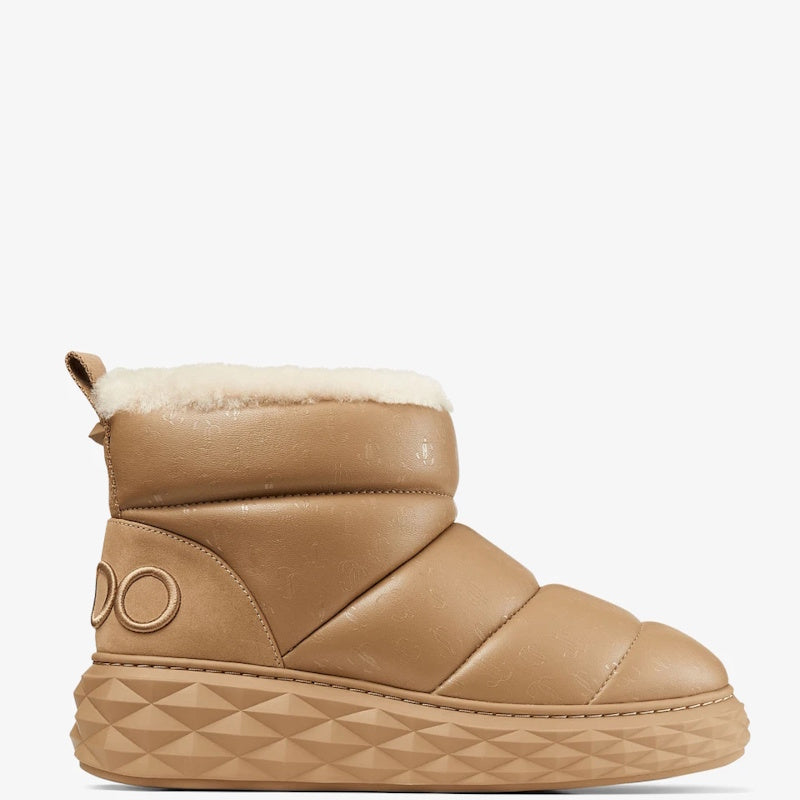 A tan mid-calf winter boot with a soft white faux-shearling lining, quilted panels, and a geometrically patterned sole, shown against a plain white background.
