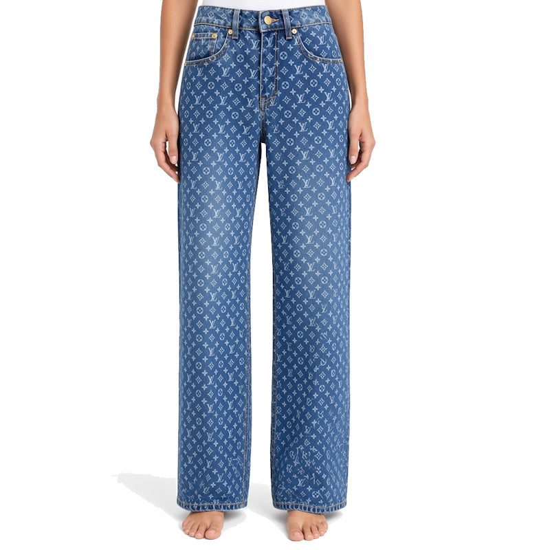 A model is shown from the waist down wearing a pair of wide-leg blue jeans featuring an all-over white monogram pattern, standing barefoot against a white background.