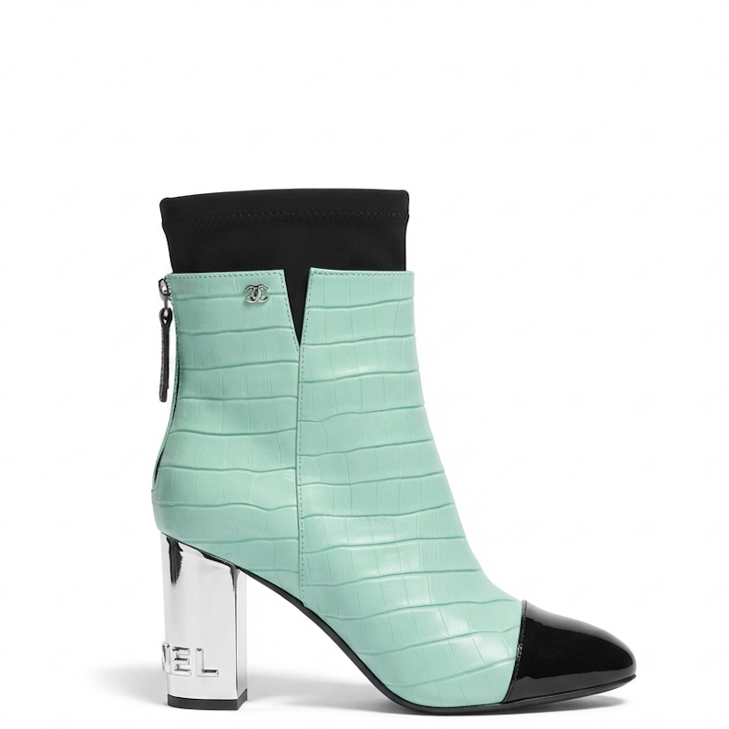 A mint green crocodile-embossed ankle boot with a black pointed toe, black elastic cuff, and a shiny silver block heel.