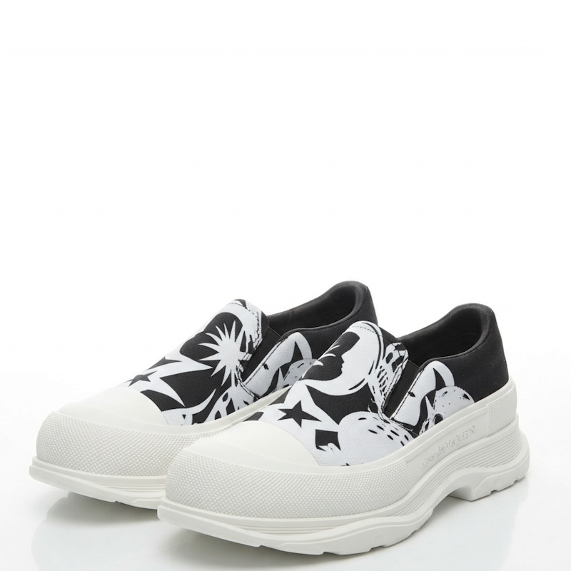 A pair of slip-on sneakers with chunky white platform soles, featuring a black and white graphic pattern on the sides and black lining.