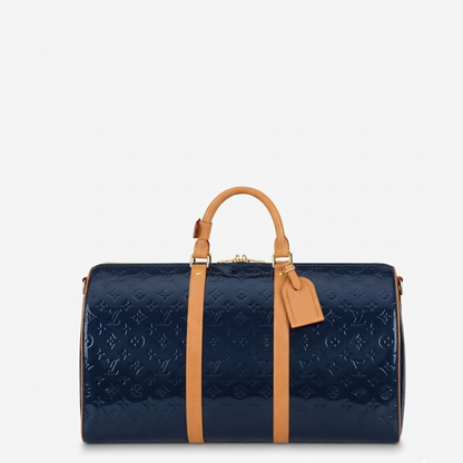  monogrammed navy blue patent leather duffel bag with tan leather handles and trim, shown against a plain light gray background.