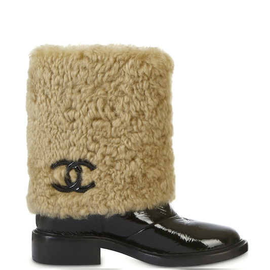  boot featuring a thick beige shearling-style cuff with a black interlocking CC logo, paired with a glossy black patent leather lower boot and block heel, shown against a plain white background.