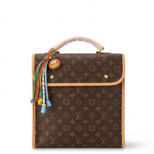 monogram canvas handbag with a beige leather handle, gold-tone hardware, and a colorful beaded tassel charm featuring a cartoon character, shown on a plain white background.