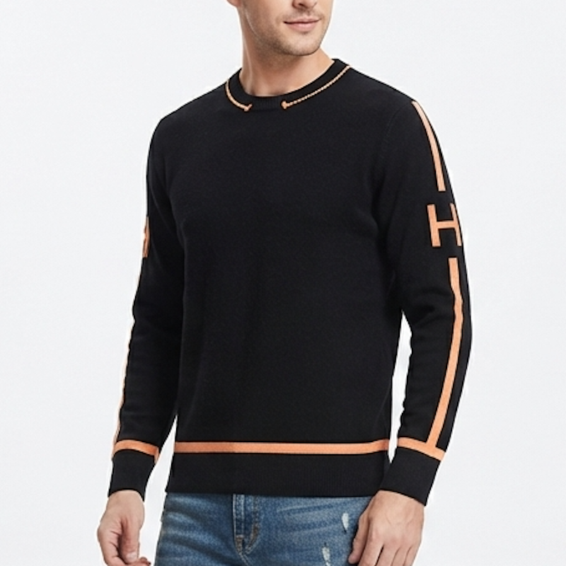 A man wearing a black crewneck sweater with contrasting orange trim and a large orange 'H' graphic on the sleeve, paired with blue jeans against a white studio background.