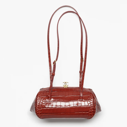 A glossy crocodile-embossed handbag in a deep reddish-brown color, featuring a single shoulder strap and a gold-tone interlocking CC turn-lock clasp on a plain white background.