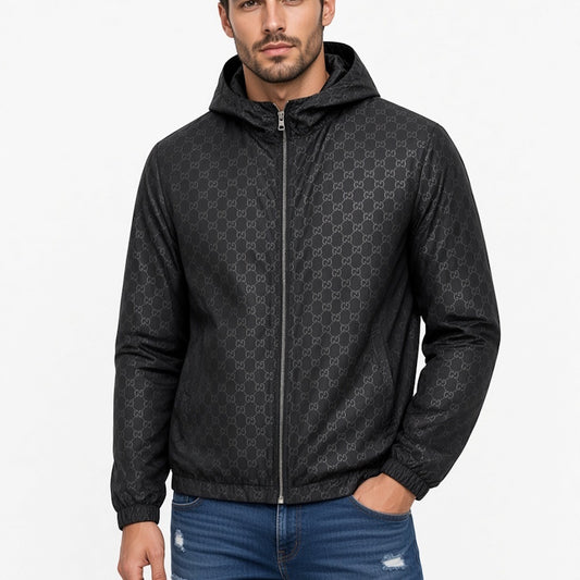 A man wearing a black hooded zip-up jacket with a subtle repeating monogram pattern, paired with blue jeans, against a plain white background.