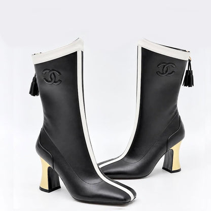 A pair of CC knee-high boots in black leather with white side stripes, black embossed CC logos, black tassel zippers, and gold block heels, shown against a light gray background.