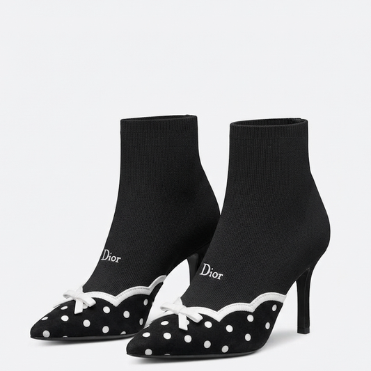 A pair of D pointed-toe heeled ankle boots in black knit fabric with white polka dots, white scalloped trim, and white bow details, shown on a light gray background.