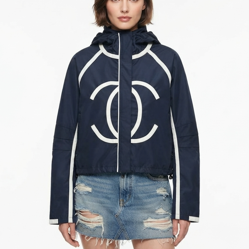 A model wearing a navy blue hooded jacket with a large white interlocking CC logo on the front, white piping details, and a white zipper, paired with a distressed denim mini skirt against a plain white background.