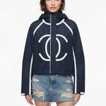 A model wearing a navy blue hooded jacket with a large white interlocking CC logo on the front, white piping details, and a white zipper, paired with a distressed denim mini skirt against a plain white background.