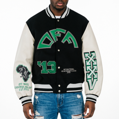 A man wearing a varsity-style jacket with a black body and off-white sleeves, featuring green collegiate lettering that reads 'DFA' and '13' on the front, plus additional green and black graphics on the sleeves, paired with distressed blue jeans against a plain white background.