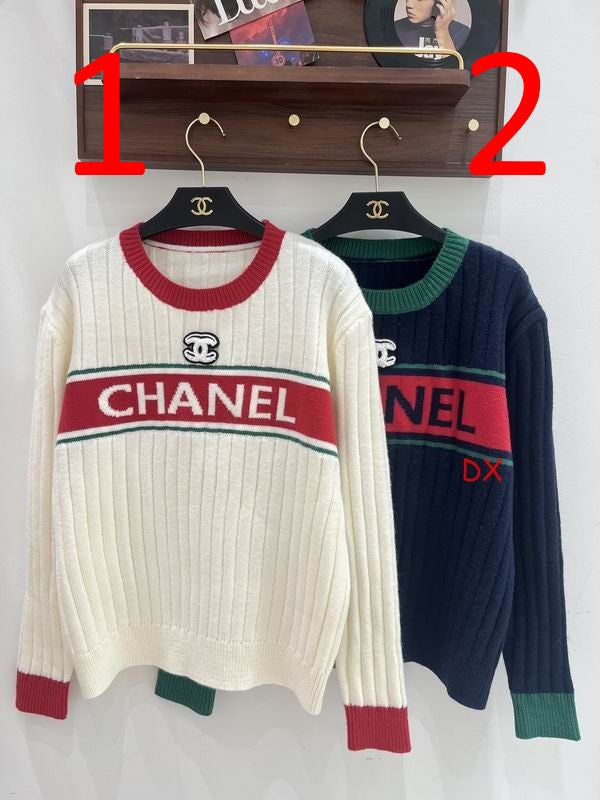 Two ribbed knit sweaters hanging on black hangers with Chanel logos, displayed against a white wall under a wooden shelf. The left sweater is cream with red and green stripes and cuffs, and the right sweater is navy with green and red stripes and cuffs.