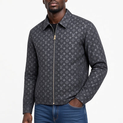 A man wearing a dark gray monogram zip-up jacket over a black shirt and blue jeans, photographed against a plain white studio background.