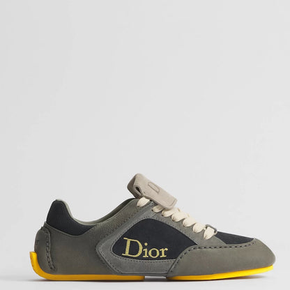 A Di low-top sneaker in olive green suede and black leather, featuring a gold Dior logo on the side, cream laces, and a bright yellow outsole, shown against a light gray background.
