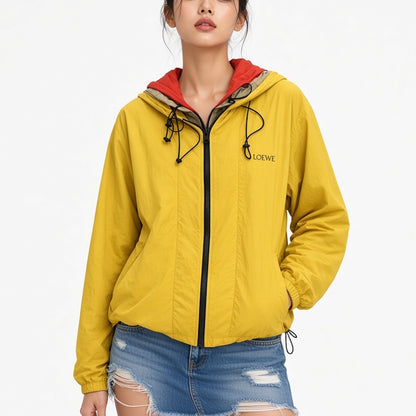A woman wearing a yellow hooded windbreaker jacket with a red inner hood lining and black zipper, paired with distressed blue jeans, against a plain white background.