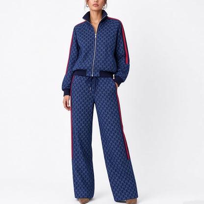 A model wearing a navy blue tracksuit with a repeating geometric monogram pattern, red side stripes, and a white zipper, photographed against a plain white studio background.