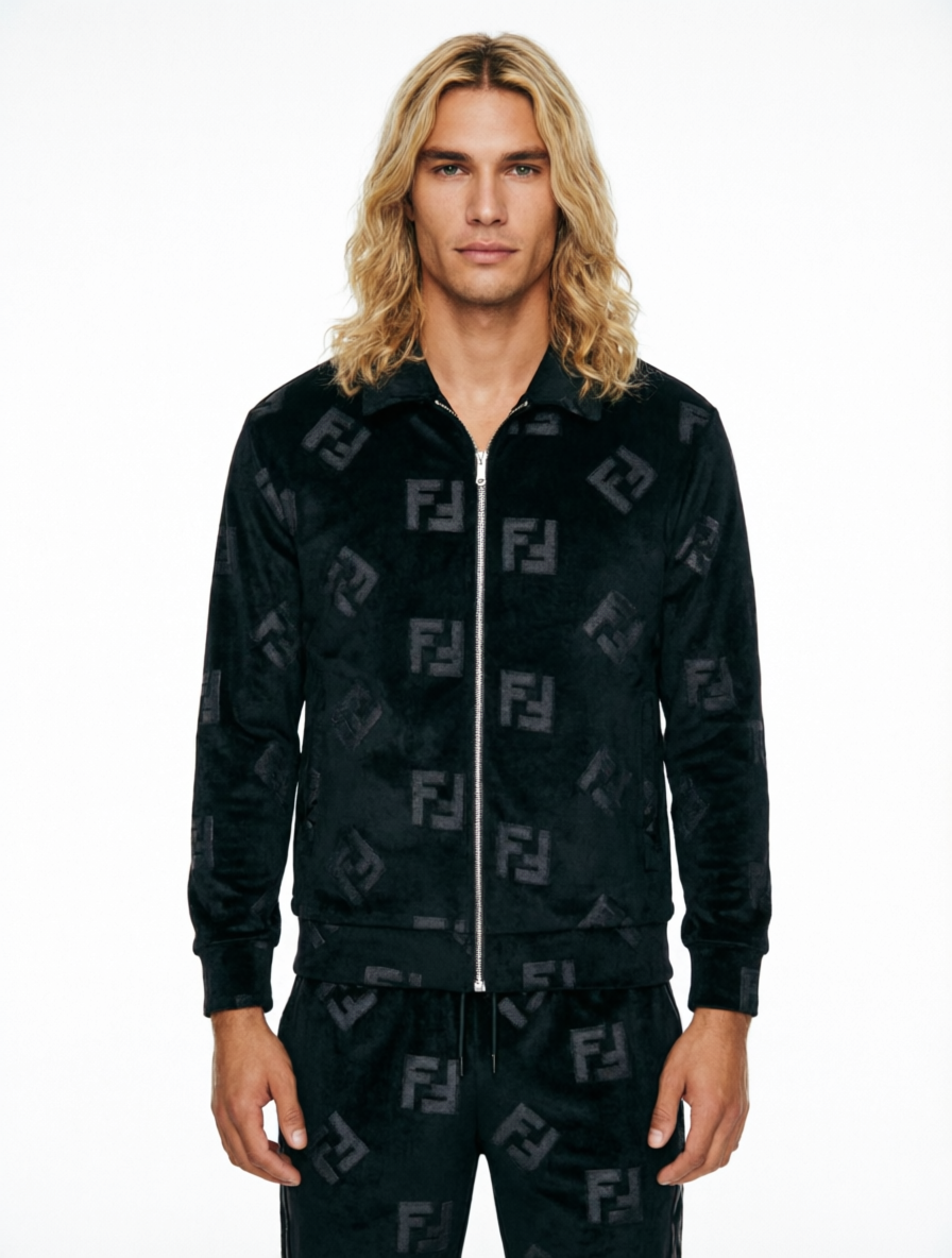 A man with long blonde hair wearing a black Fendi velour tracksuit with an allover tonal FF logo pattern, featuring a zip-up jacket and matching pants, against a plain white background.