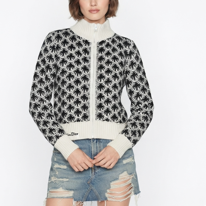 A model wearing a black and off-white knit zip-up cardigan with a palm tree pattern, paired with a distressed denim mini skirt. The cardigan features a mock neck, ribbed cuffs, and a visible Dior logo on the left sleeve.