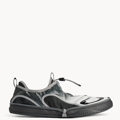 A low-top slip-on sneaker in a glossy black and silver gradient finish, featuring a zippered closure and a textured black sole, shown against a plain white background.