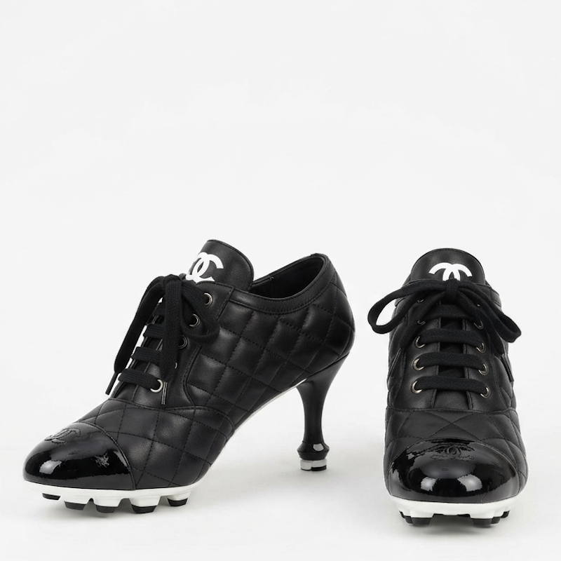 A pair of black quilted high-heeled fashion shoes with patent leather toe caps, black laces, and white sole details, displayed on a clean white background.