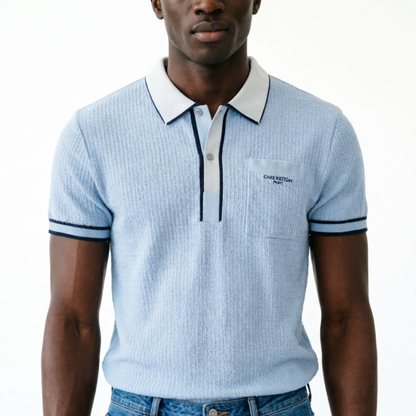 A man wearing a light blue ribbed short-sleeve polo shirt with a white collar and navy blue trim, featuring the '' logo on the chest pocket.