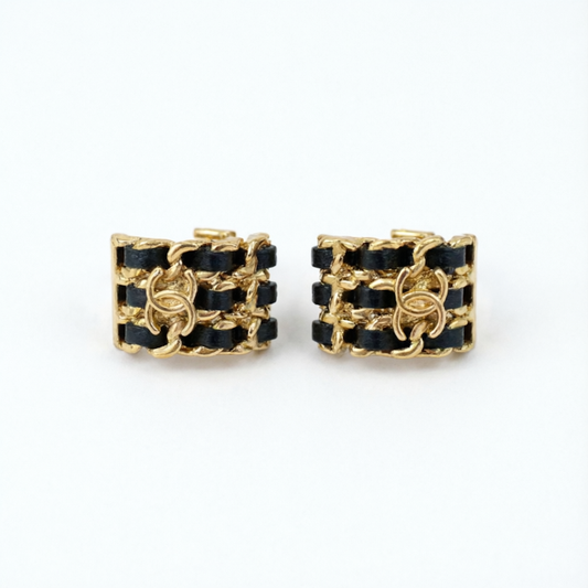 A pair of gold-tone chain-link cuff earrings with black woven ribbon detailing, displayed on a clean white background.