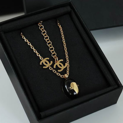 A gold-tone necklace with a double-C logo pendant and a black oval pendant featuring a gold heart, displayed inside a black presentation box.