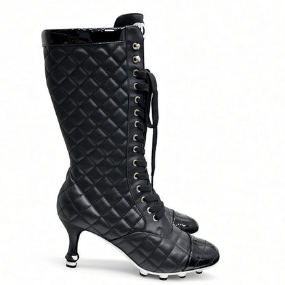 A black quilted knee-high boot with a pointed toe, kitten heel, and silver metal studs down the side, shown against a plain white background.