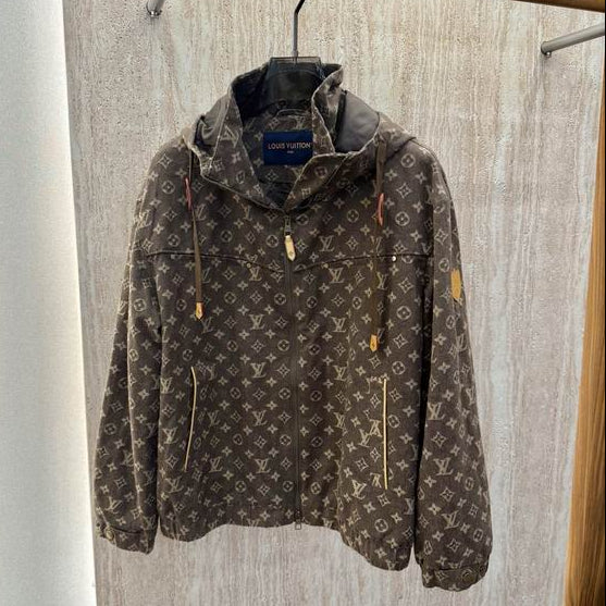 A L monogram hooded jacket in brown and beige canvas, hanging on a black hanger from a clothing rack against a light wood-paneled wall.