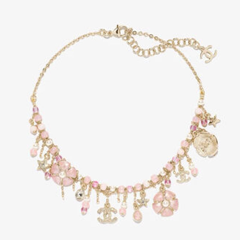 A gold-tone statement necklace featuring pink beads, floral charms, star charms, and interlocking CC logo charms, displayed on a light gray background.