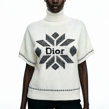 A model wearing a cream-colored short-sleeve turtleneck sweater with a black geometric Di logo on the chest.