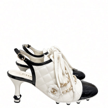 A pair of  high-heeled slingback shoes featuring a white quilted leather body, black patent leather toe caps and heel accents, white laces, and gold-tone chain and floral hardware.