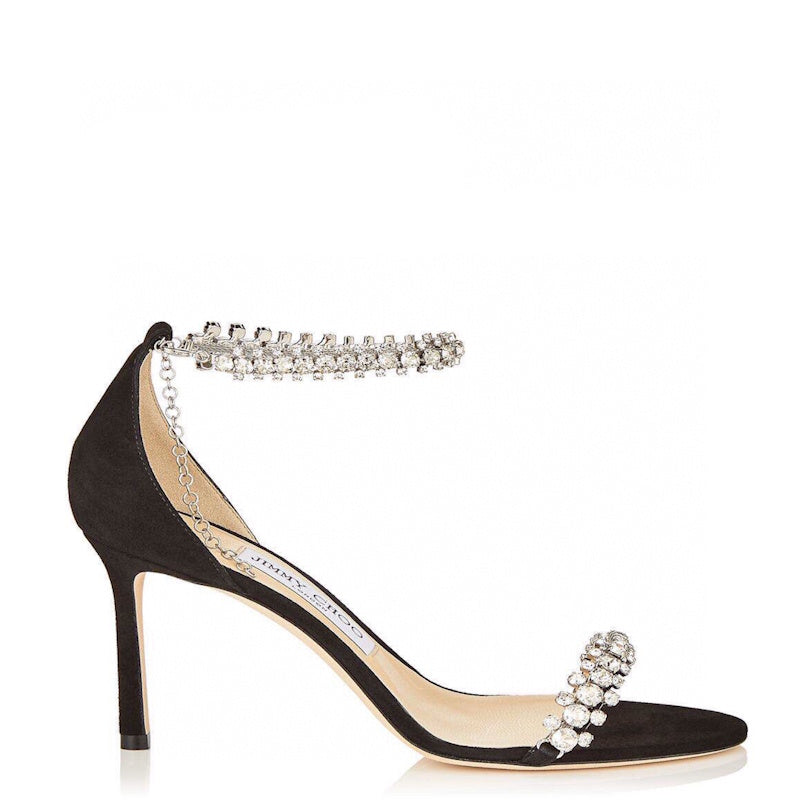 A single black suede high-heeled pump with a pointed toe, a slim stiletto heel, and a delicate chain strap adorned with sparkling clear crystals around the ankle and toe, shown against a plain white background.