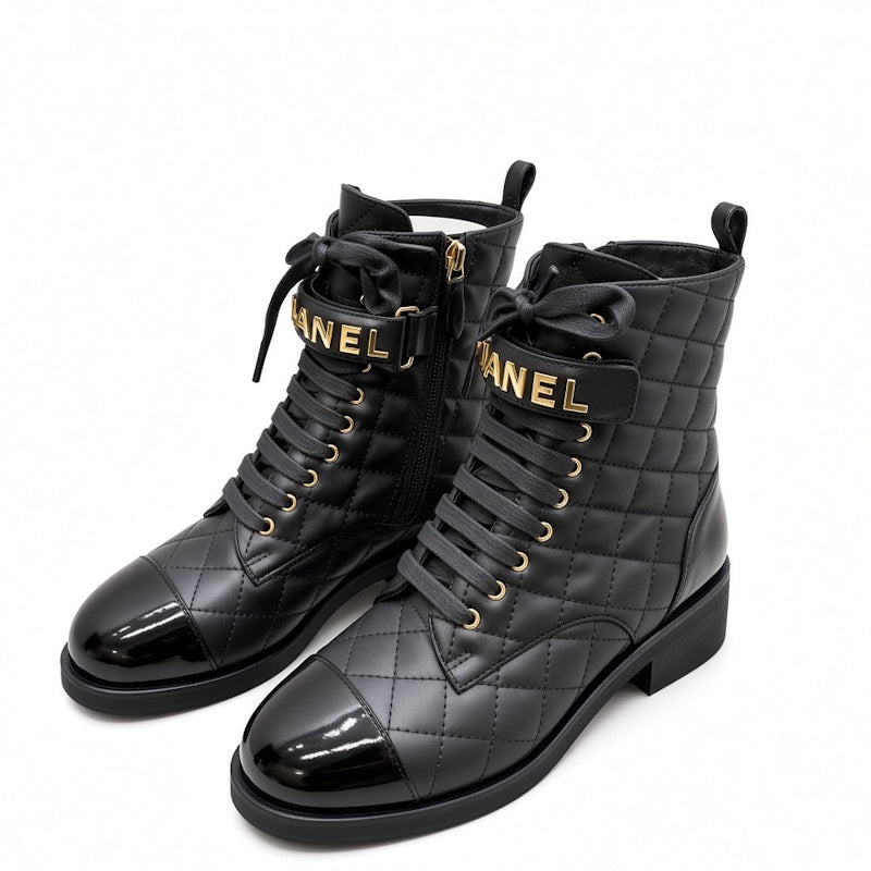 A pair of black quilted combat boots with patent leather toes, black laces, and gold-tone hardware. The straps feature the brand name  in gold lettering, and the boots are set against a plain white background.