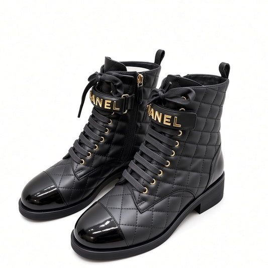 A pair of black quilted combat boots with patent leather toes, black laces, and gold-tone hardware. The straps feature the brand name  in gold lettering, and the boots are set against a plain white background.