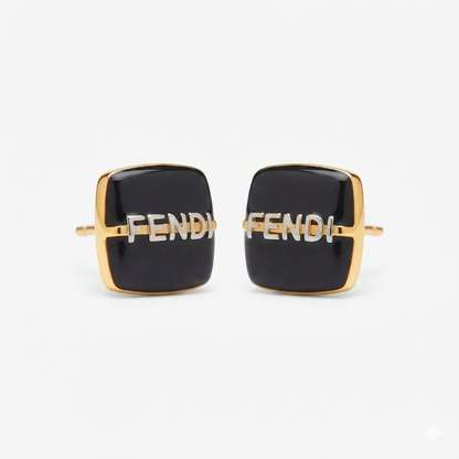 A pair of Fendi square cufflinks with black enamel faces, gold-tone metal borders, and the Fendi logo in silver-tone lettering across the center, set against a plain light gray background.