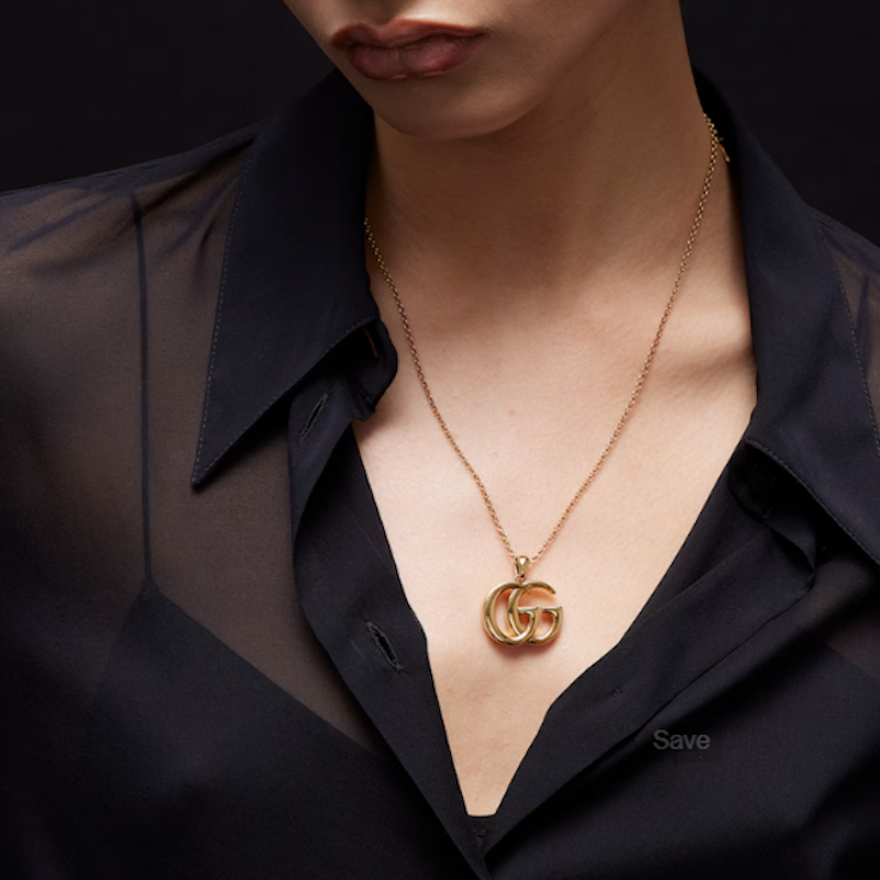 A close-up of a model wearing a gold chain necklace with a double-G logo pendant, styled with a black satin shirt.